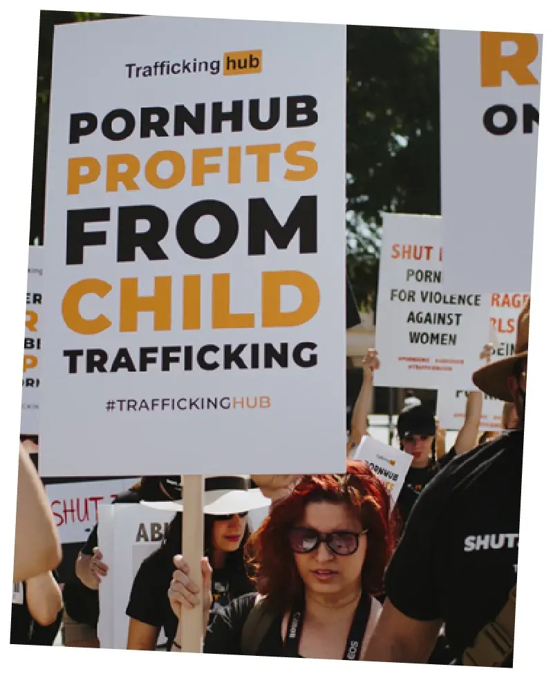A woman with black tape on her mouth holds up a Traffickinghub sign at a protest